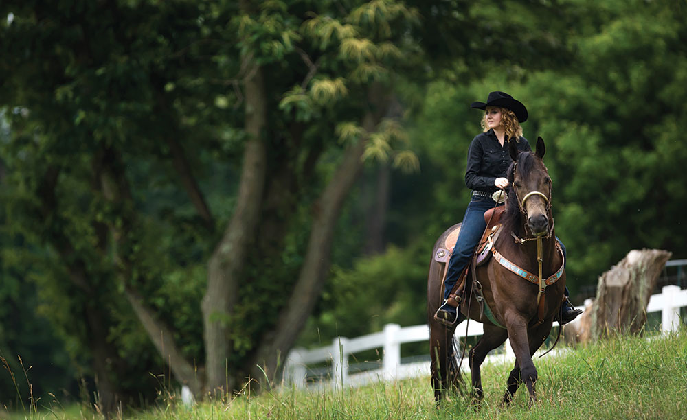 Danielle Thompson riding a horse along a fence.